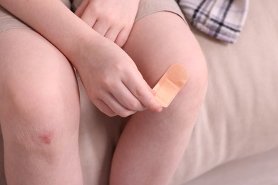 Photo of Little boy putting sticking plaster onto knee on sofa, closeup