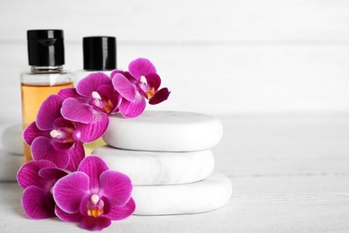 Spa stones, bottles and orchid flowers on white wooden table. Space for text