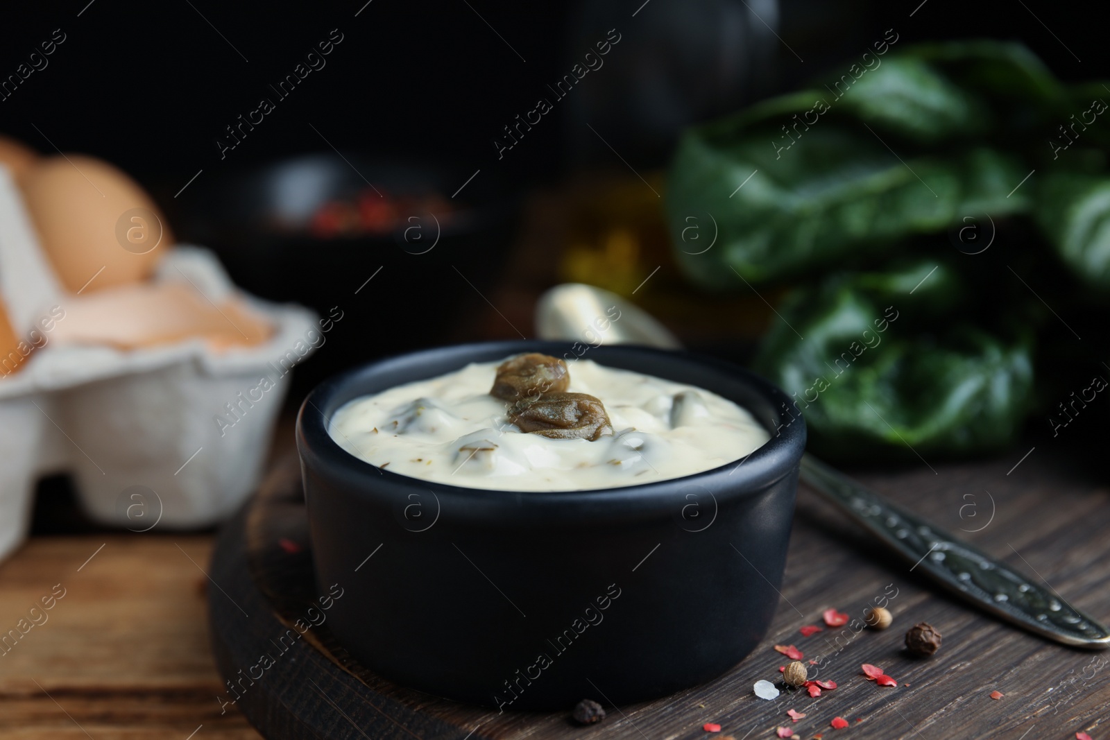 Photo of Caper sauce in bowl on wooden table, closeup