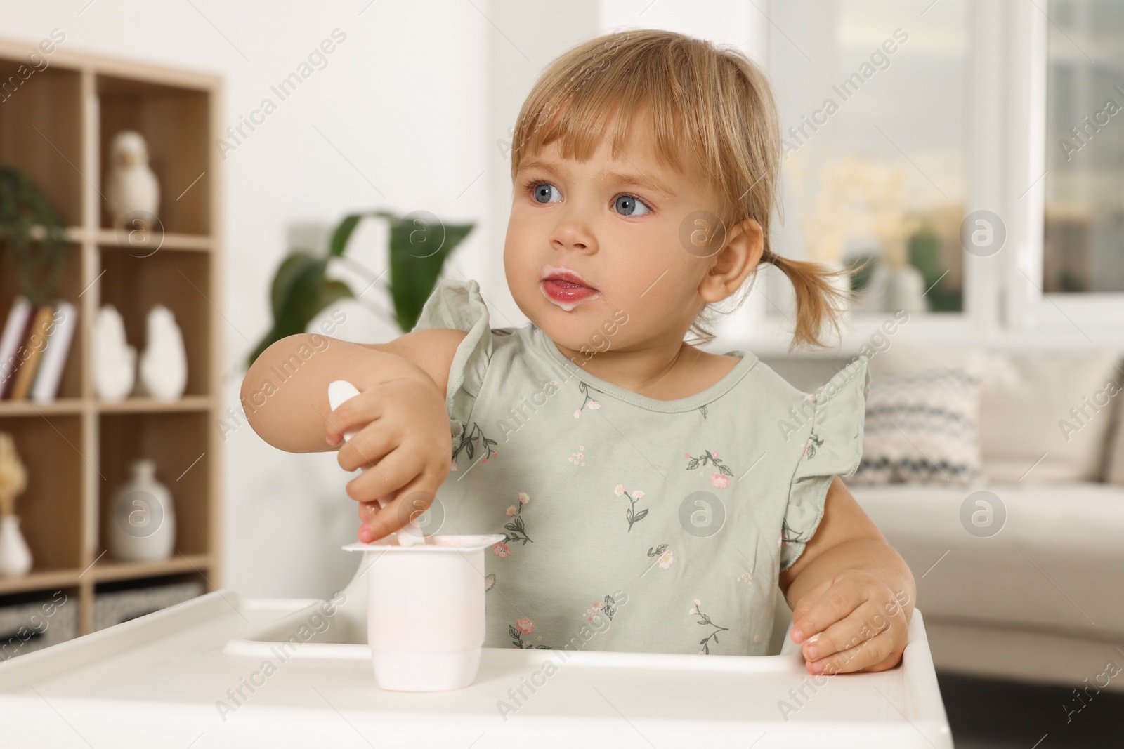 Photo of Cute little child eating tasty yogurt with spoon at home