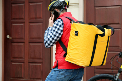 Photo of Courier with thermo bag and mobile phone near customer's house. Food delivery service