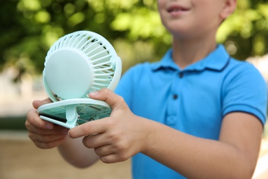 Little boy with portable fan outdoors, closeup. Summer heat