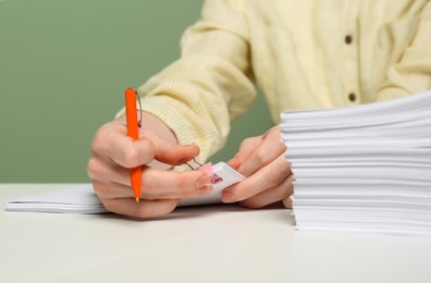 Woman signing documents at white table against green background, closeup