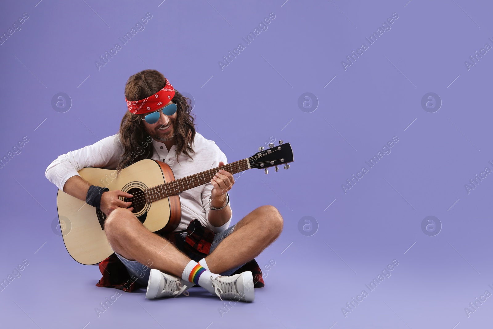 Photo of Stylish hippie man with guitar on violet background, space for text