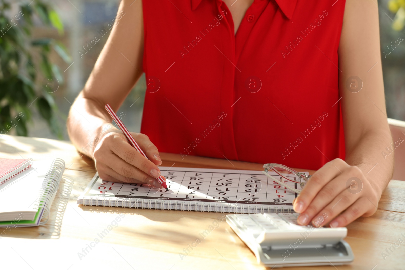 Photo of Woman marking date in calendar at wooden table, closeup