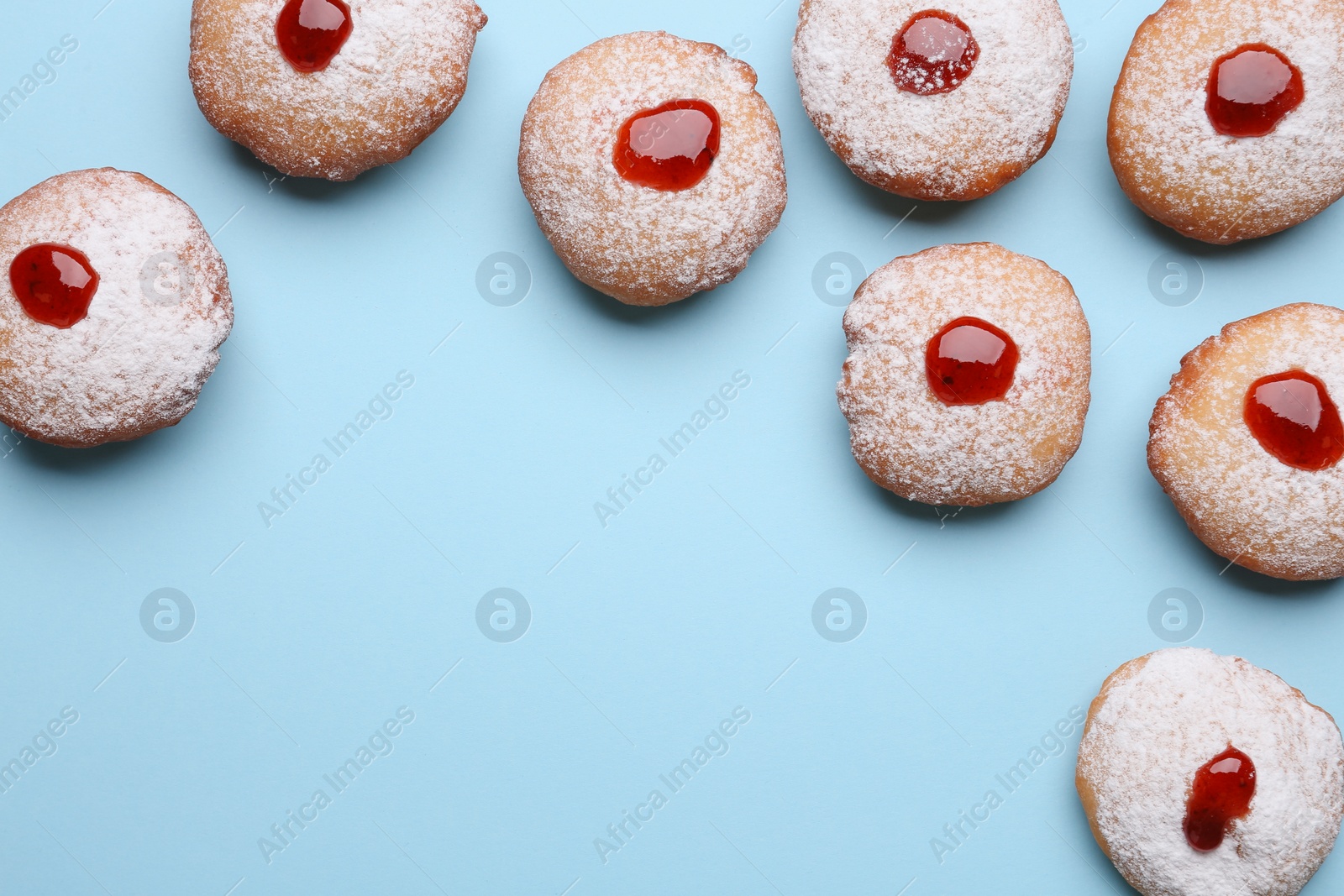 Photo of Hanukkah donuts with jelly and powdered sugar on light blue background, flat lay. Space for text