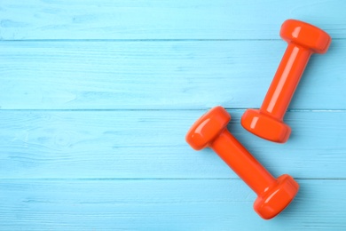 Bright dumbbells and space for text on wooden background, flat lay. Home fitness