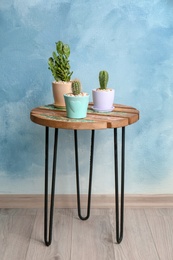 Photo of Beautiful cacti on table against color wall