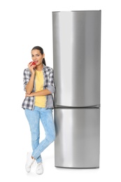 Photo of Young woman eating apple near closed refrigerator on white background