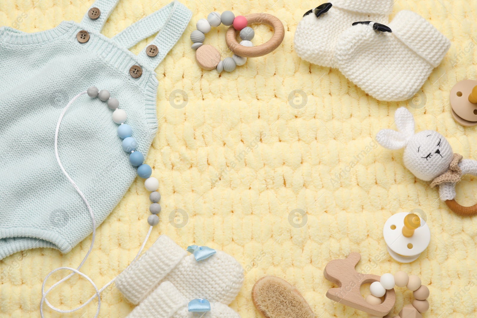 Photo of Frame of cute baby stuff on yellow knitted fabric, flat lay. Space for text