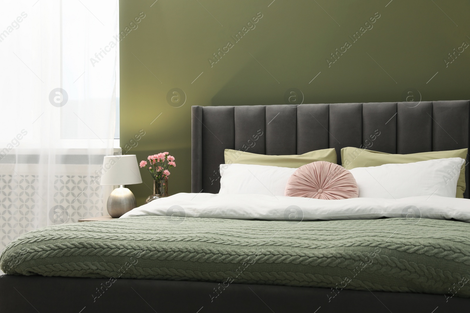 Photo of Large comfortable bed, lamp and beautiful flowers in stylish room. Interior design