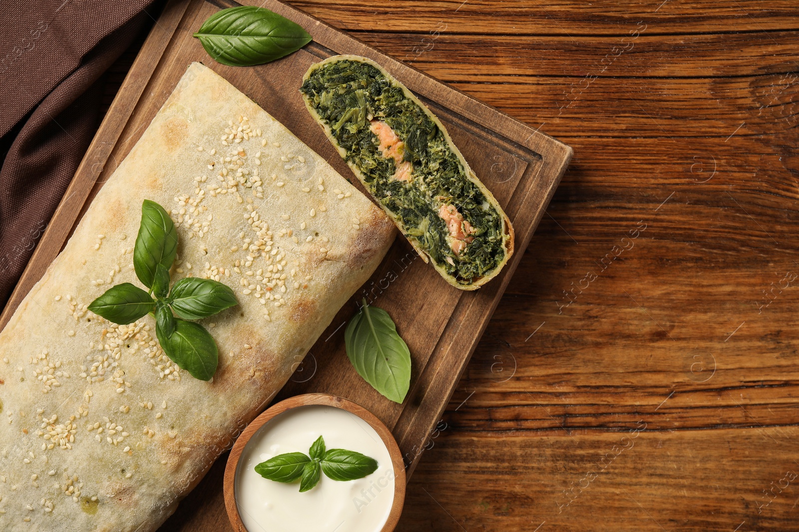 Photo of Cut tasty strudel with salmon, spinach, basil and sauce on wooden table, top view