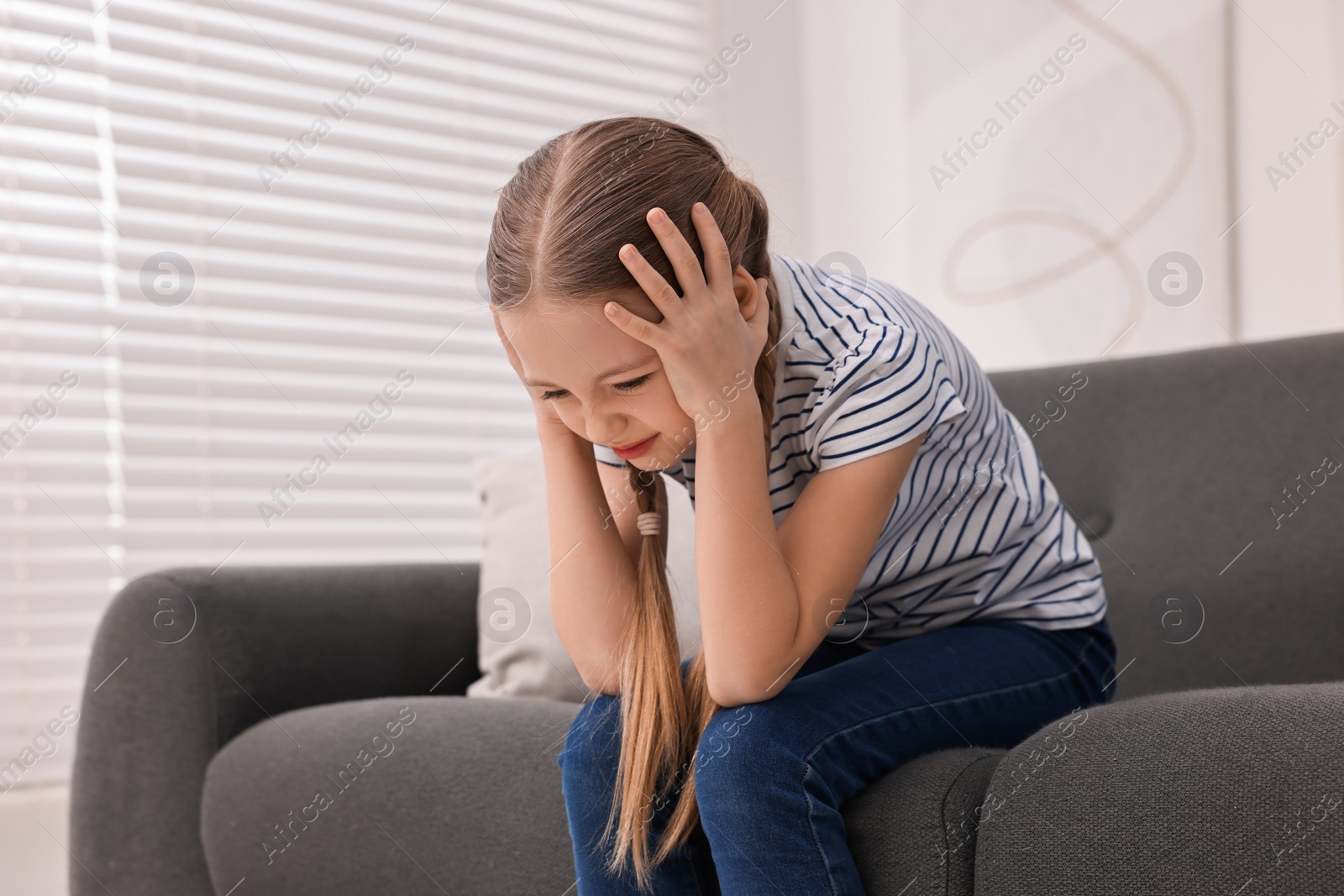 Photo of Little girl suffering from headache on sofa indoors