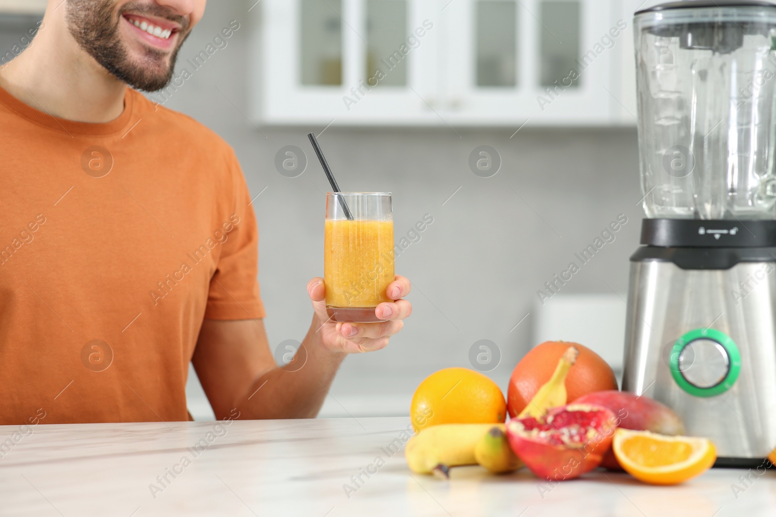 Photo of Man with delicious smoothie at white marble table in kitchen, closeup