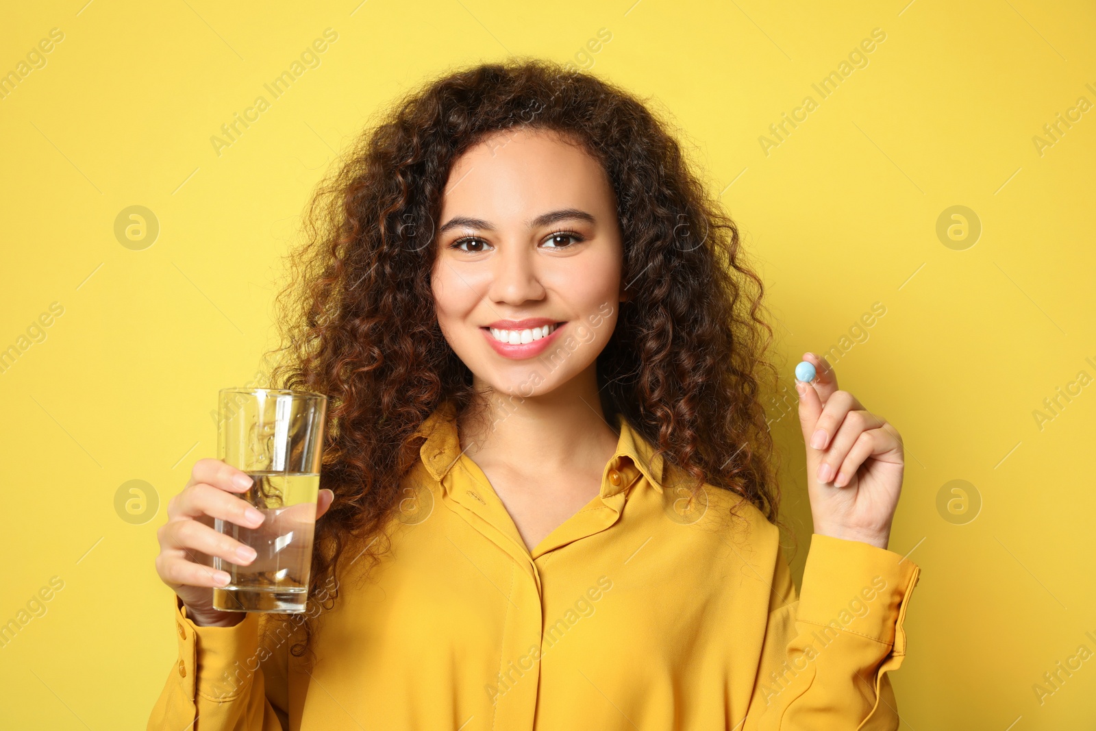 Photo of African-American woman with glass of water and vitamin pill on yellow background