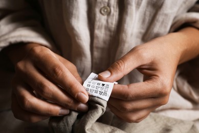 Photo of Woman holding clothing label on beige garment, closeup