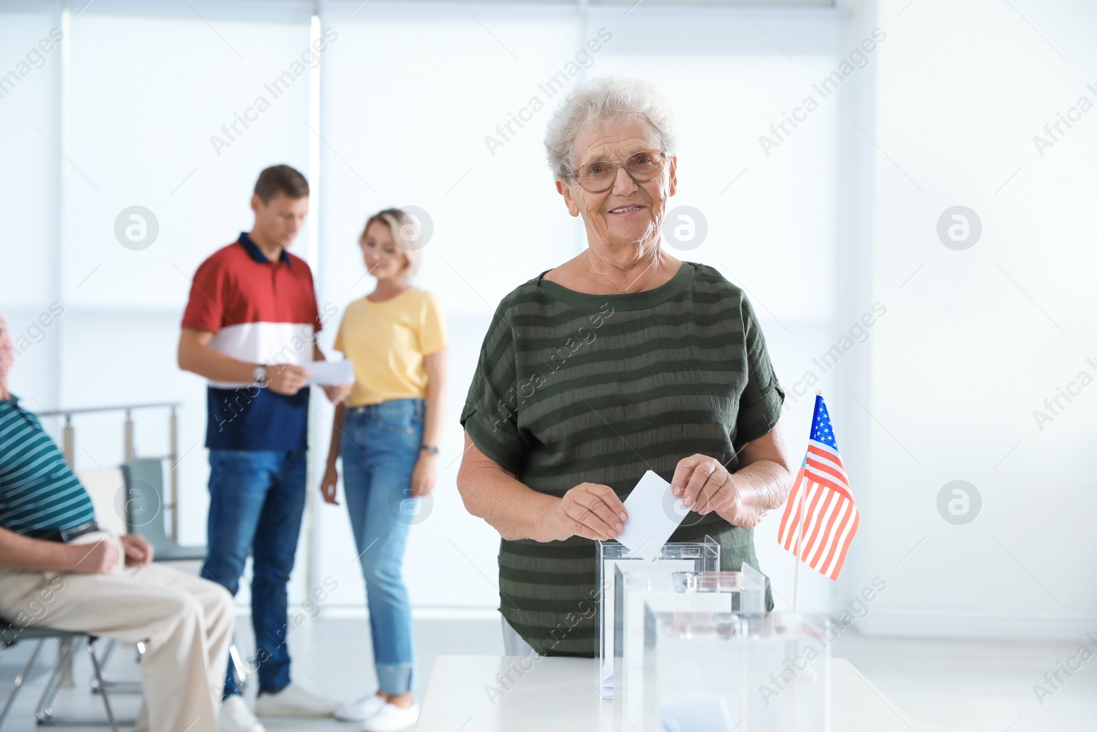 Photo of Elderly woman putting ballot paper into box at polling station