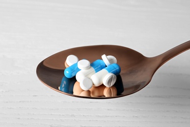 Photo of Spoon with weight loss pills on light background