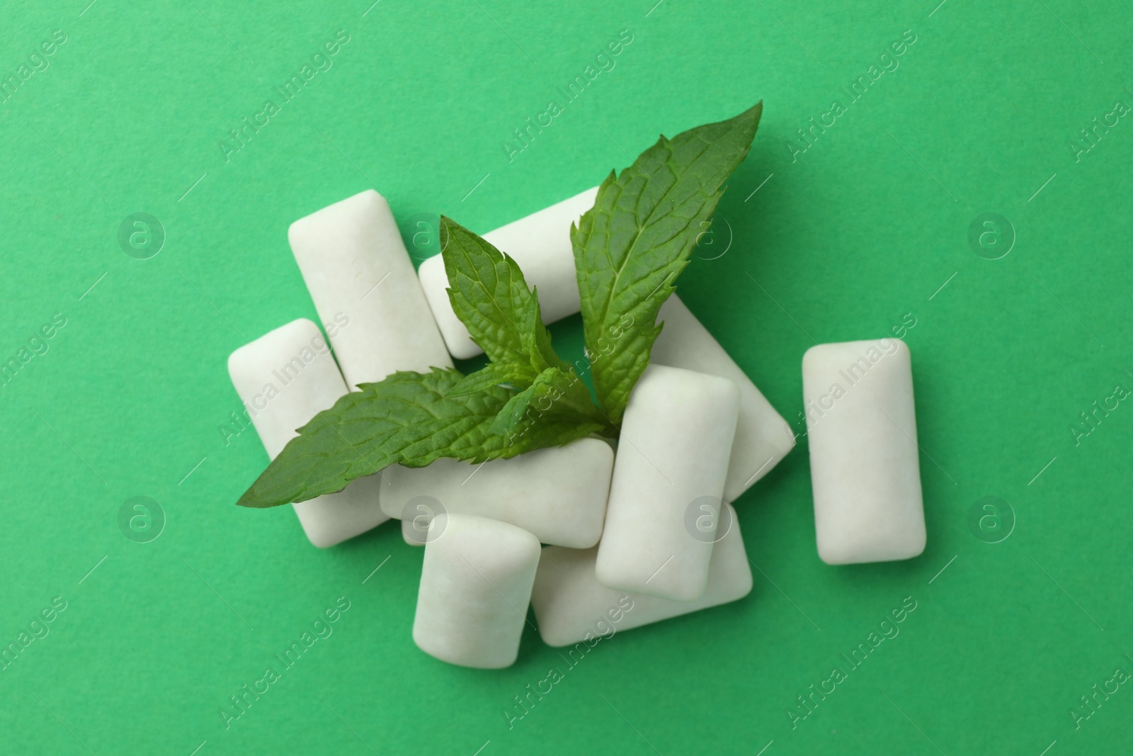 Photo of Tasty white chewing gums and mint leaves on green background, top view