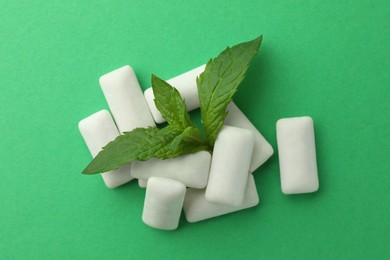 Photo of Tasty white chewing gums and mint leaves on green background, top view