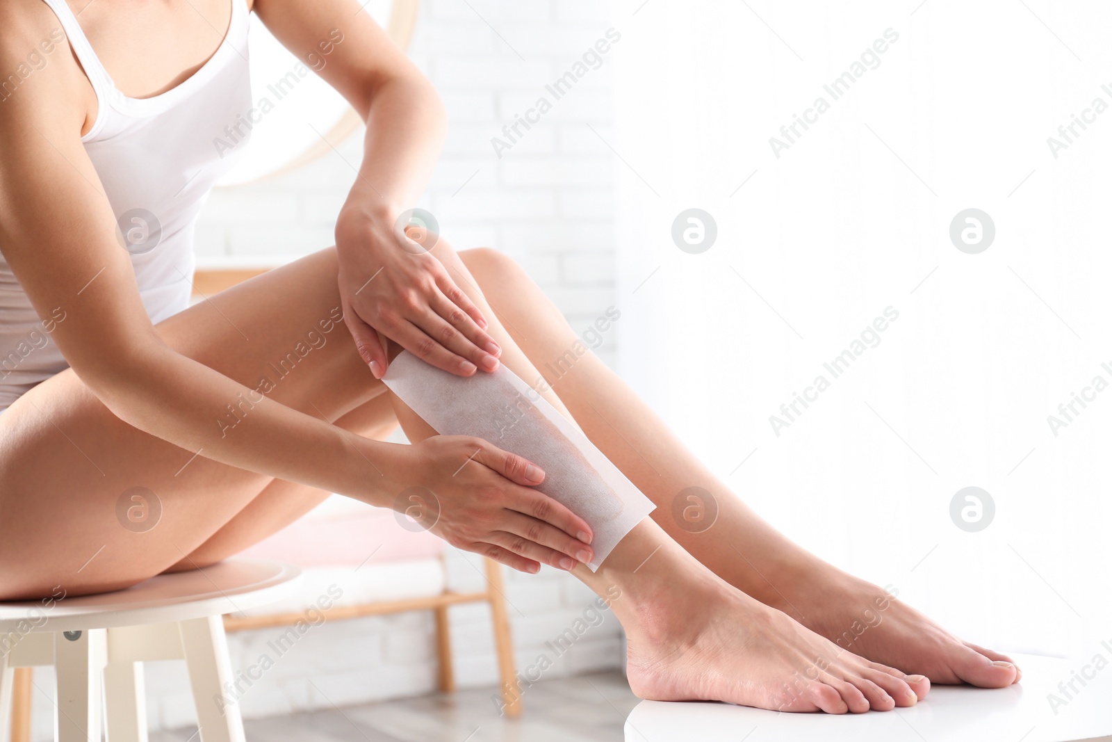 Photo of Woman doing leg epilation procedure with wax strips indoors, closeup