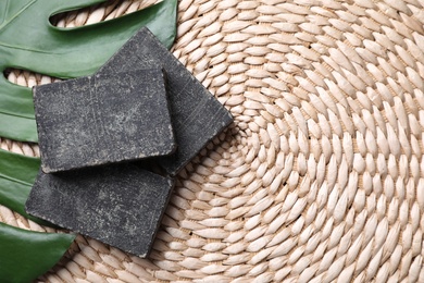 Photo of Natural tar soap on wicker mat with green leaf, flat lay. Space for text