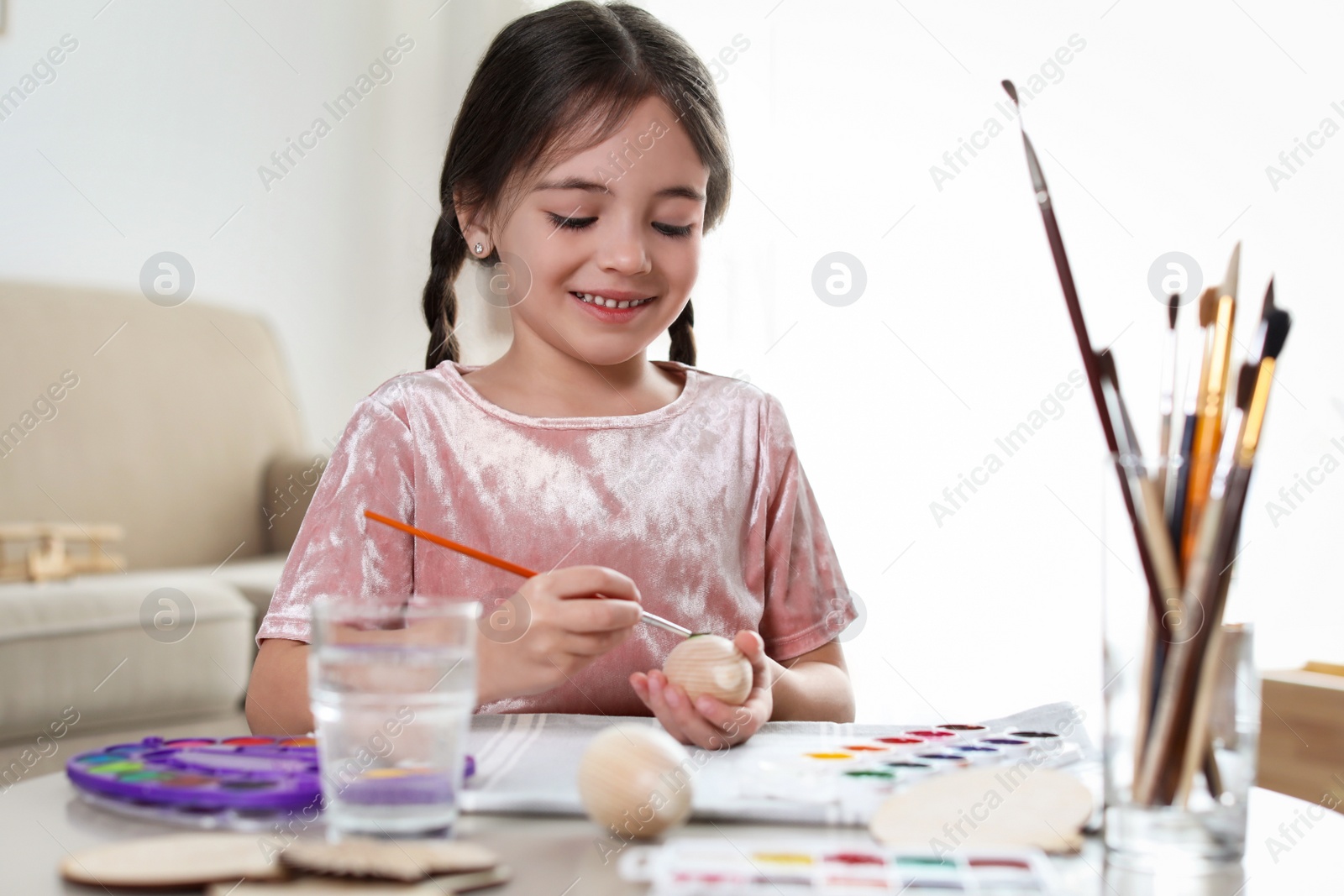 Photo of Little girl painting decorative egg at table indoors. Creative hobby