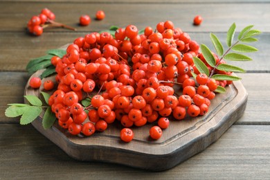 Photo of Board with fresh ripe rowan berries and leaves on wooden table