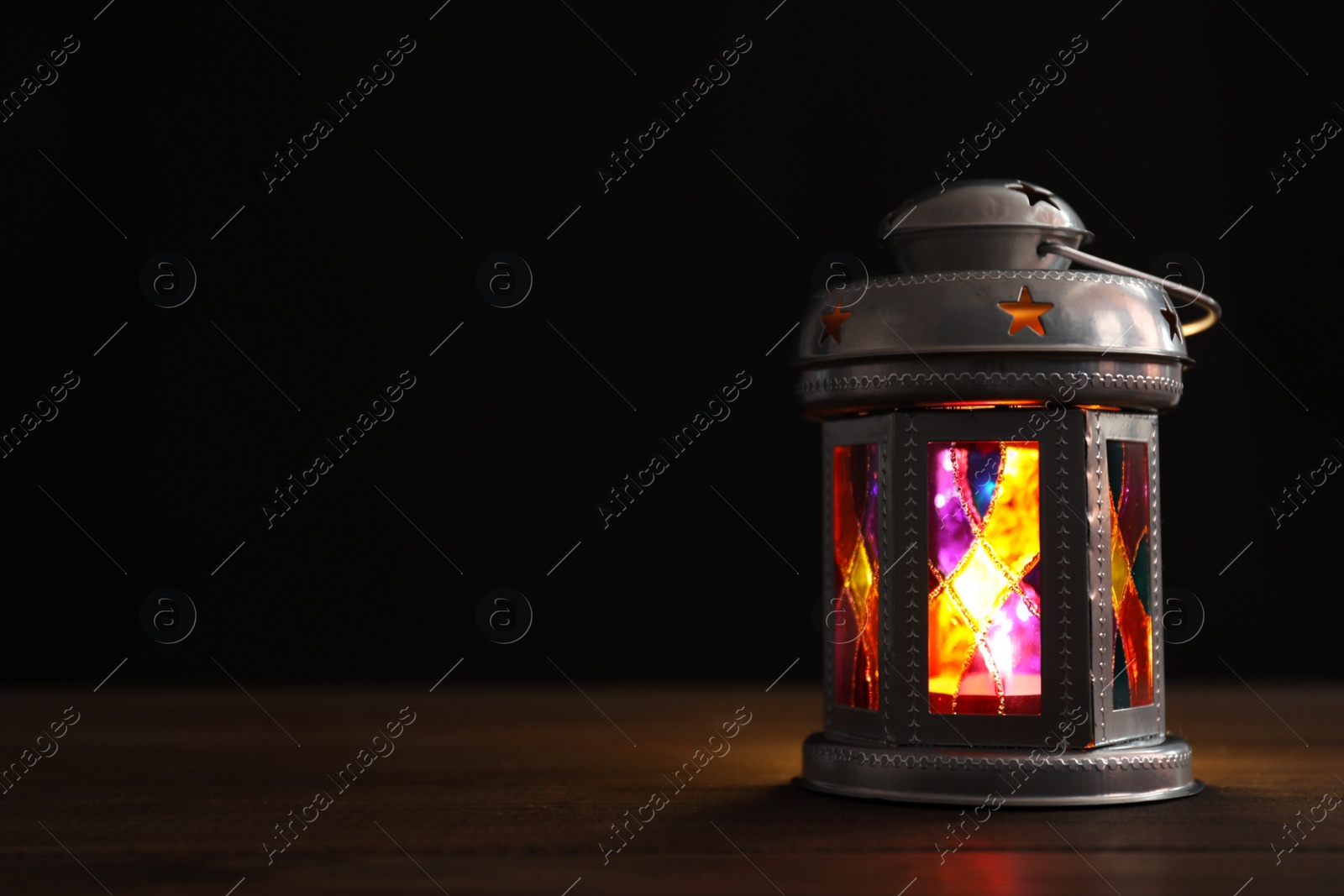 Photo of Decorative Arabic lantern on wooden table against black background, space for text