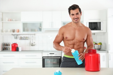 Young shirtless athletic man preparing protein shake in kitchen, space for text