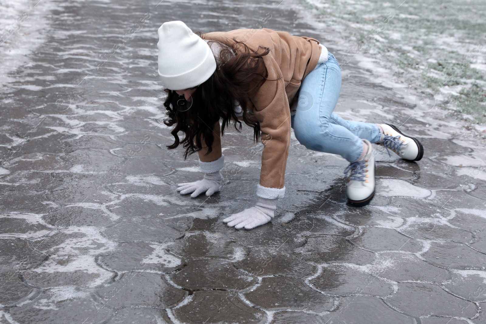 Photo of Young woman trying to stand up after falling on slippery icy pavement outdoors