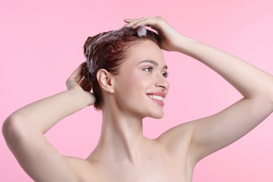 Happy young woman washing her hair with shampoo on pink background