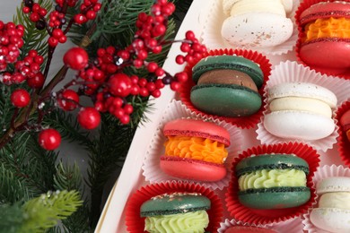 Photo of Different tasty Christmas macarons in box and festive decor on table, top view