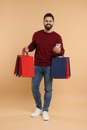 Smiling man with many paper shopping bags and smartphone on beige background