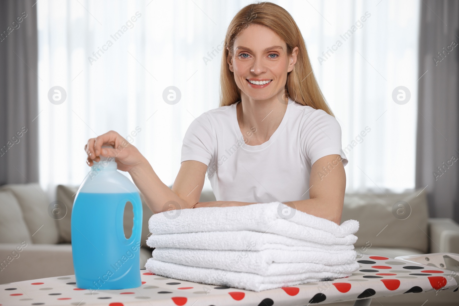 Photo of Woman with fabric softener and clean towels in room, space for text