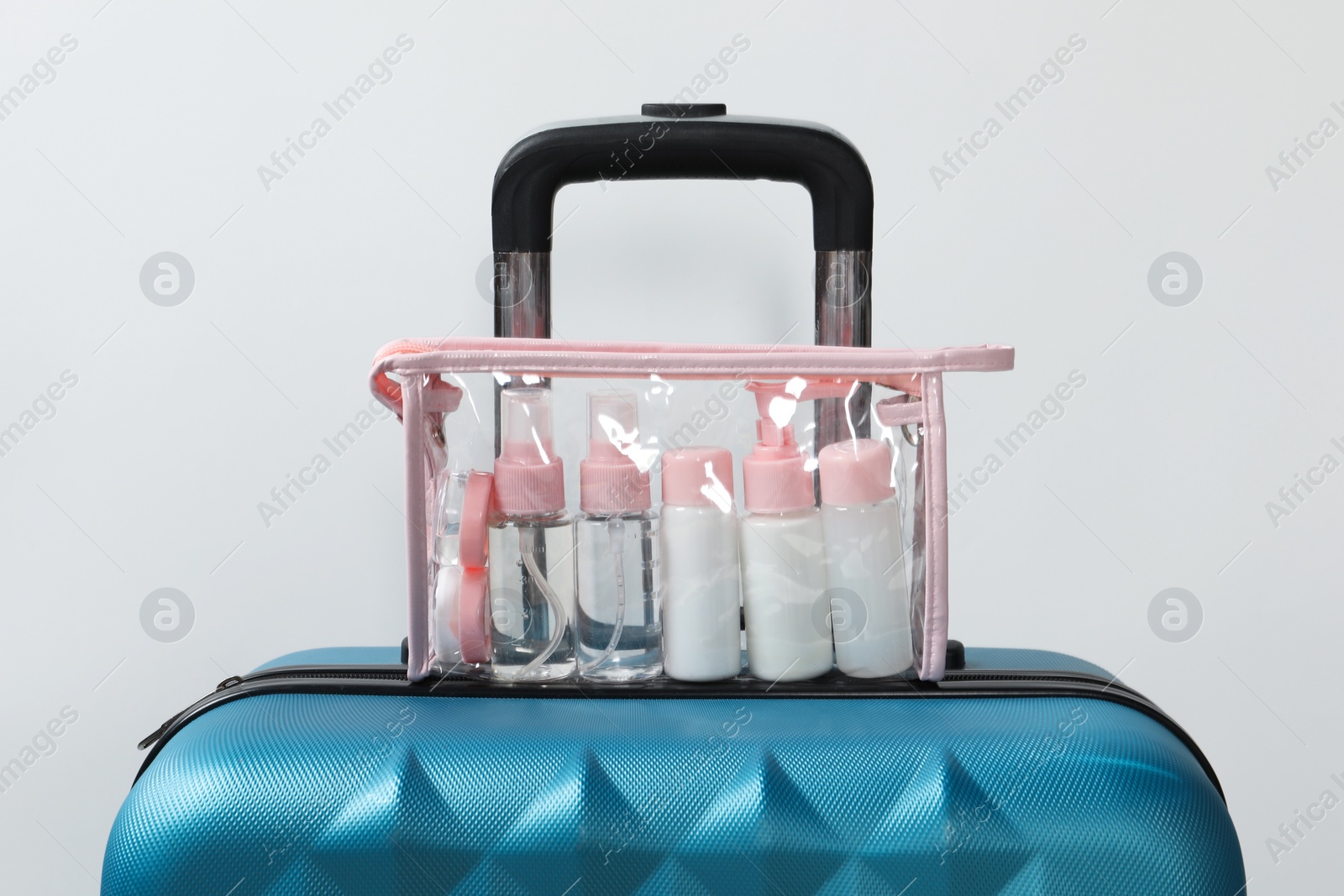 Photo of Cosmetic travel kit in plastic bag on suitcase against light background