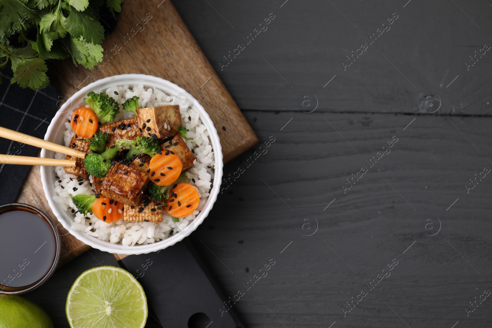Photo of Delicious rice with fried tofu, broccoli and carrots served on grey wooden table, flat lay. Space for text