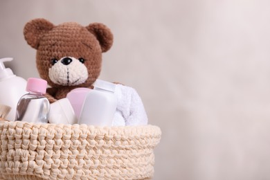 Photo of Baby cosmetic products, bath accessories and toy bear in knitted basket on beige background, closeup. Space for text