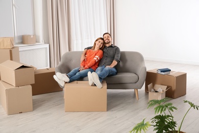 Photo of Couple resting on sofa near moving boxes in their new house