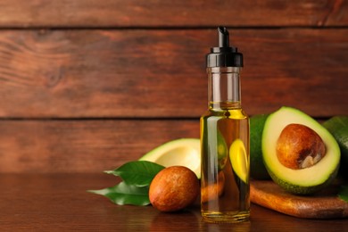 Photo of Glass bottle of cooking oil and fresh avocados on wooden table, space for text