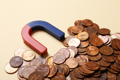 Photo of Magnet attracting coins on beige background, closeup