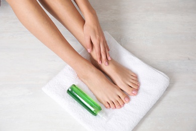 Photo of Woman with smooth feet, white towel and cosmetic on light background, top view. Spa treatment