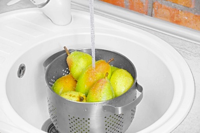 Photo of Fresh ripe pears under tap water in kitchen sink