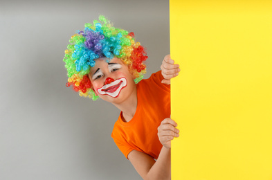 Photo of Preteen boy with clown wig looking out of yellow banner on light grey background, space for text. April fool's day