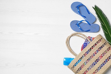 Flat lay composition with beach bag and accessories on white wooden background, space for text