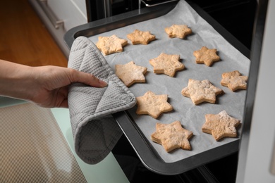 Photo of Woman taking baking tray with tasty Christmas cookies out of oven
