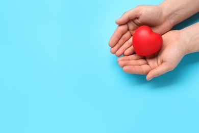 Photo of Man holding red decorative heart on light blue background, top view and space for text. Cardiology concept