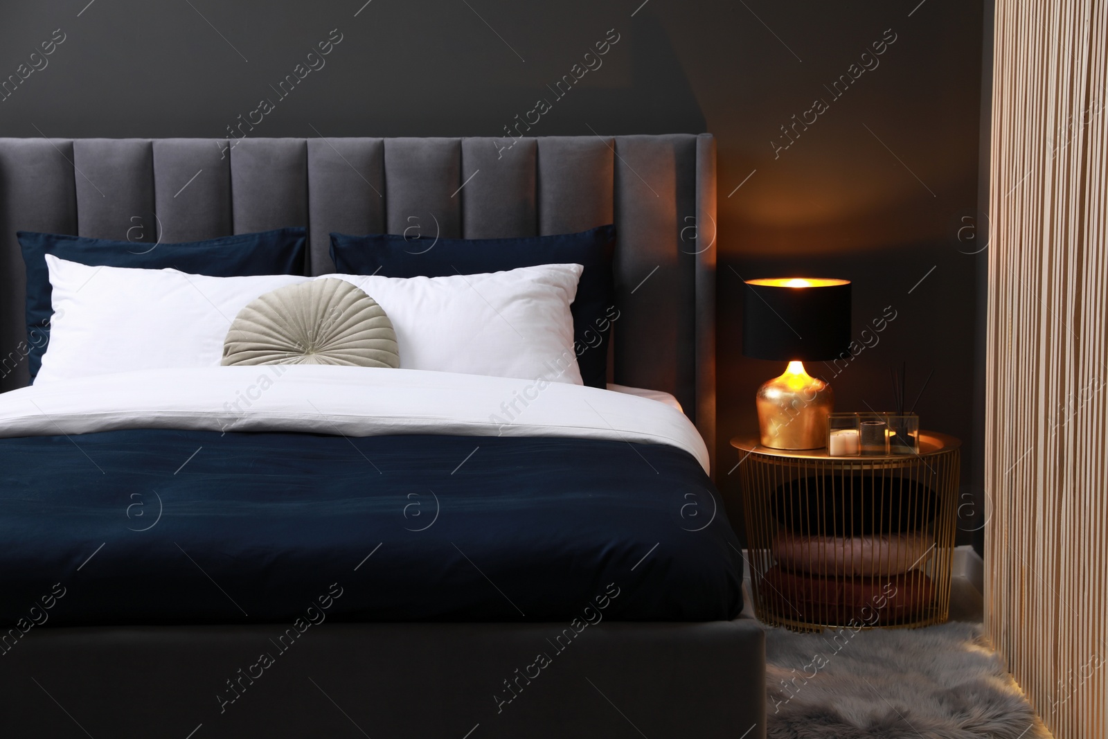 Photo of Comfortable bed with cushions, lamp and different decor on bedside table in room. Stylish interior
