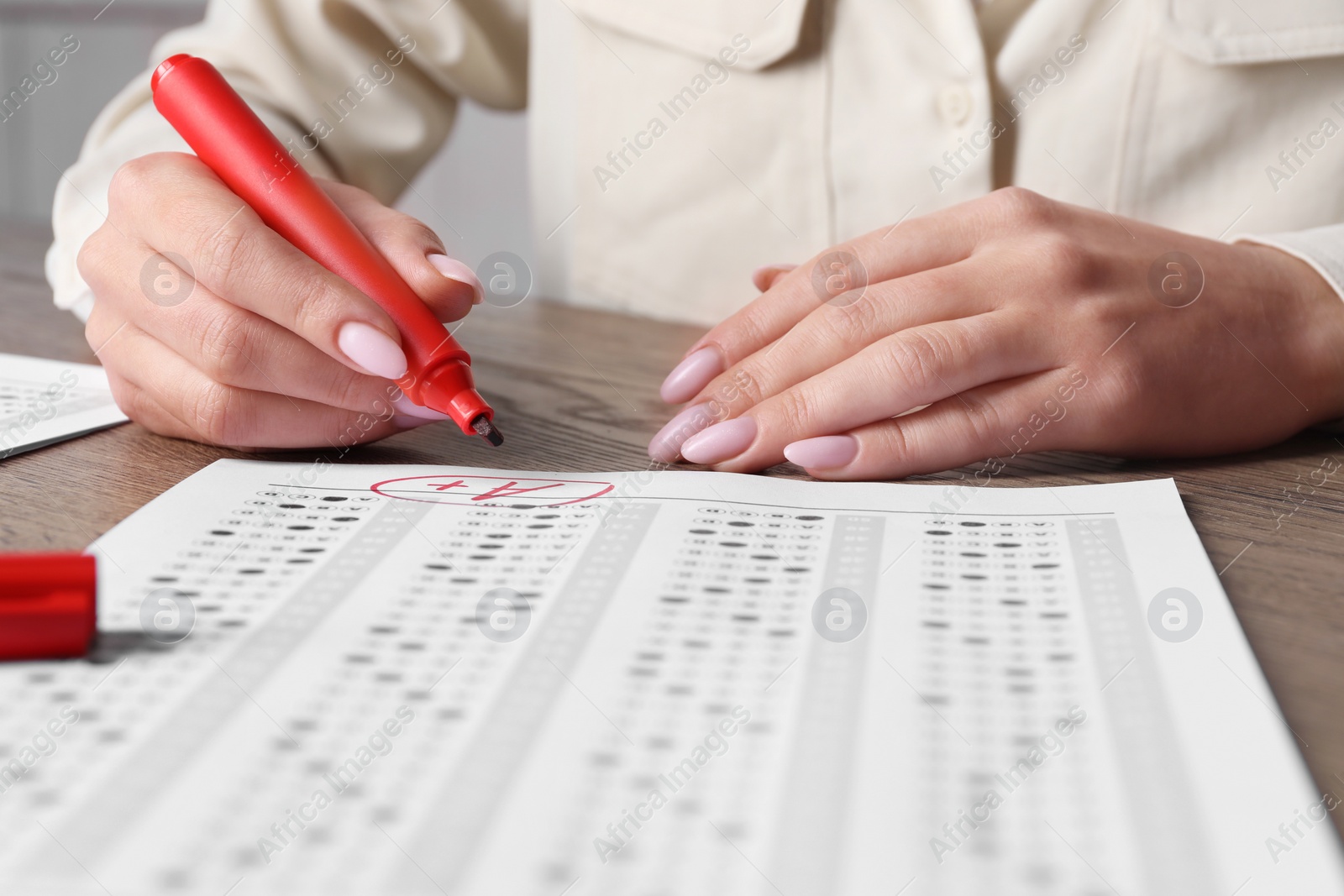 Photo of School grade. Teacher writing letter A with plus symbol on answer sheet at wooden table, closeup