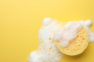Photo of Sponge with foam on yellow background, top view. Space for text
